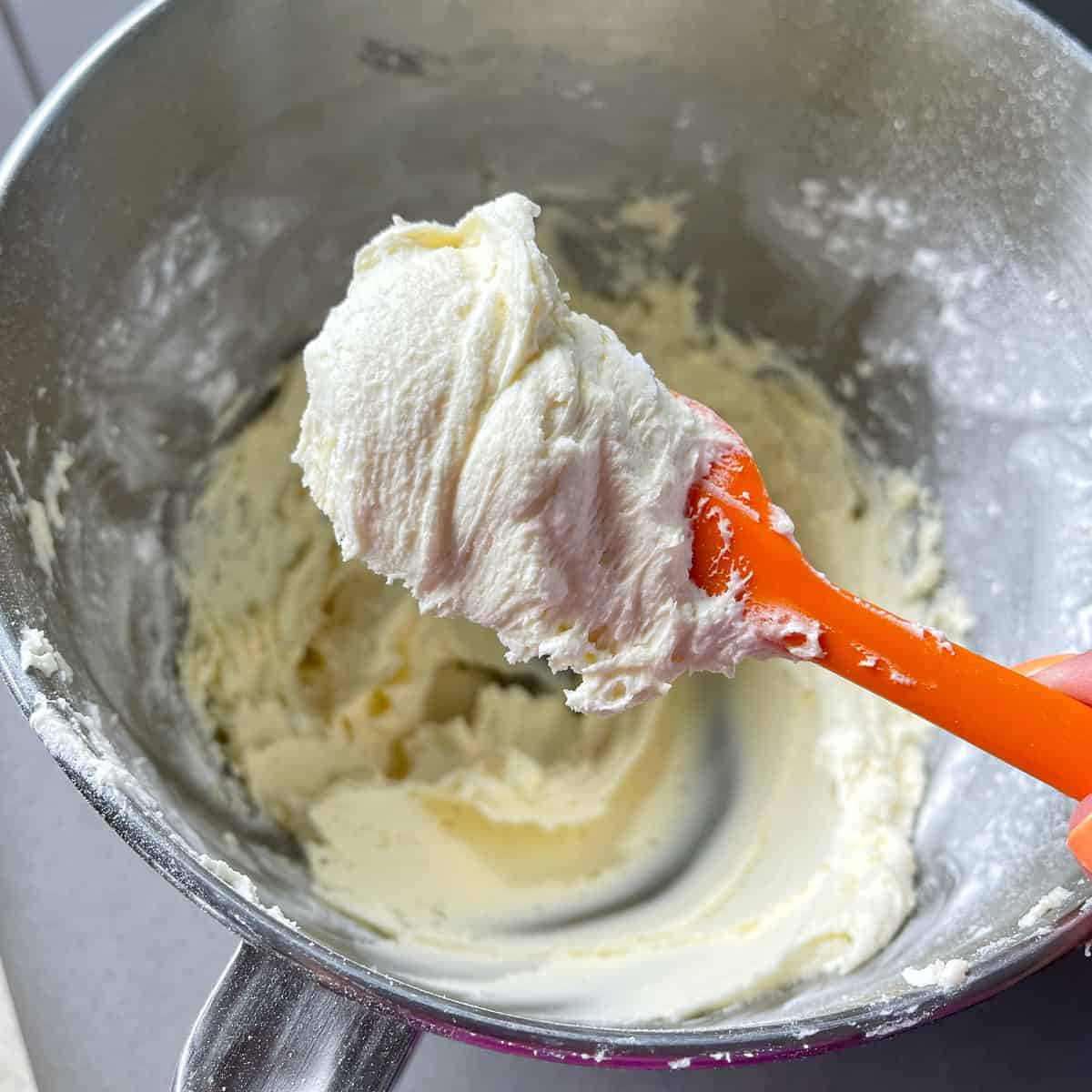 Buttercream icing on an orange spatula over a mixing bowl.
