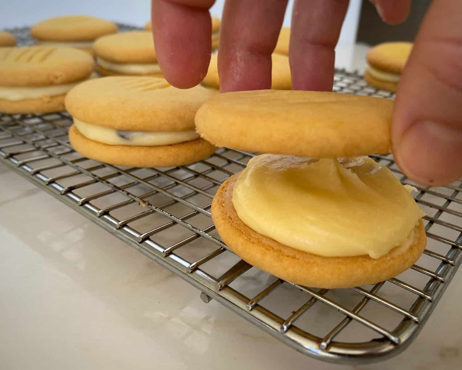  A hand sandwiching two biscuits together with icing.