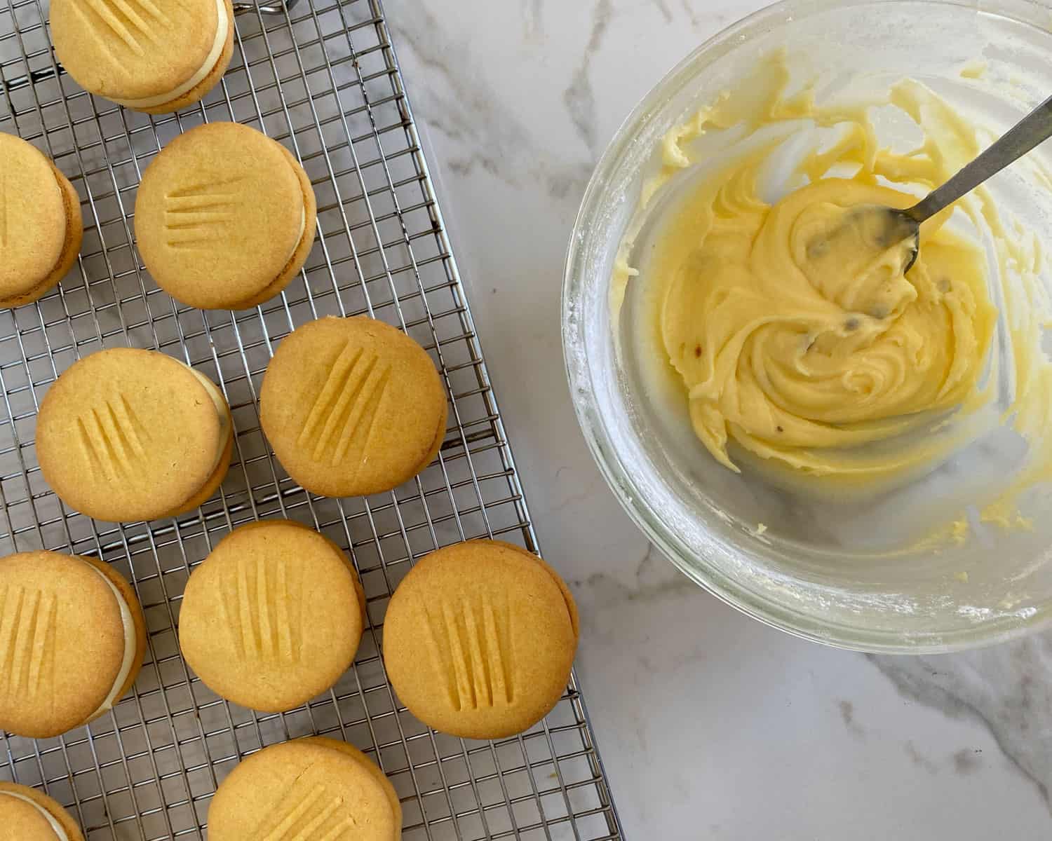 Cooked biscuits on a wire rack next to icing in a glass bowl.