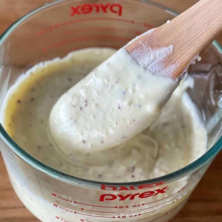 Cheese sauce in a glass pyrex jug being stirred by a wooden spoon.