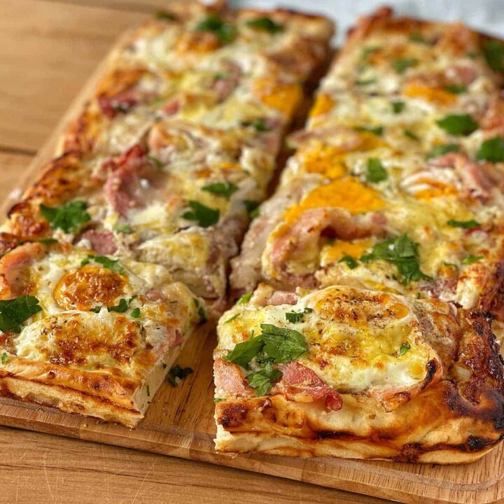 a large piece of breakfast pizza slab on a wooden chopping board