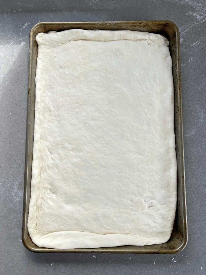 Breakfast Pizza Slab A rectangular baking pan filled with uncooked Breakfast Pizza Slab dough spread evenly to the edges on a gray countertop.