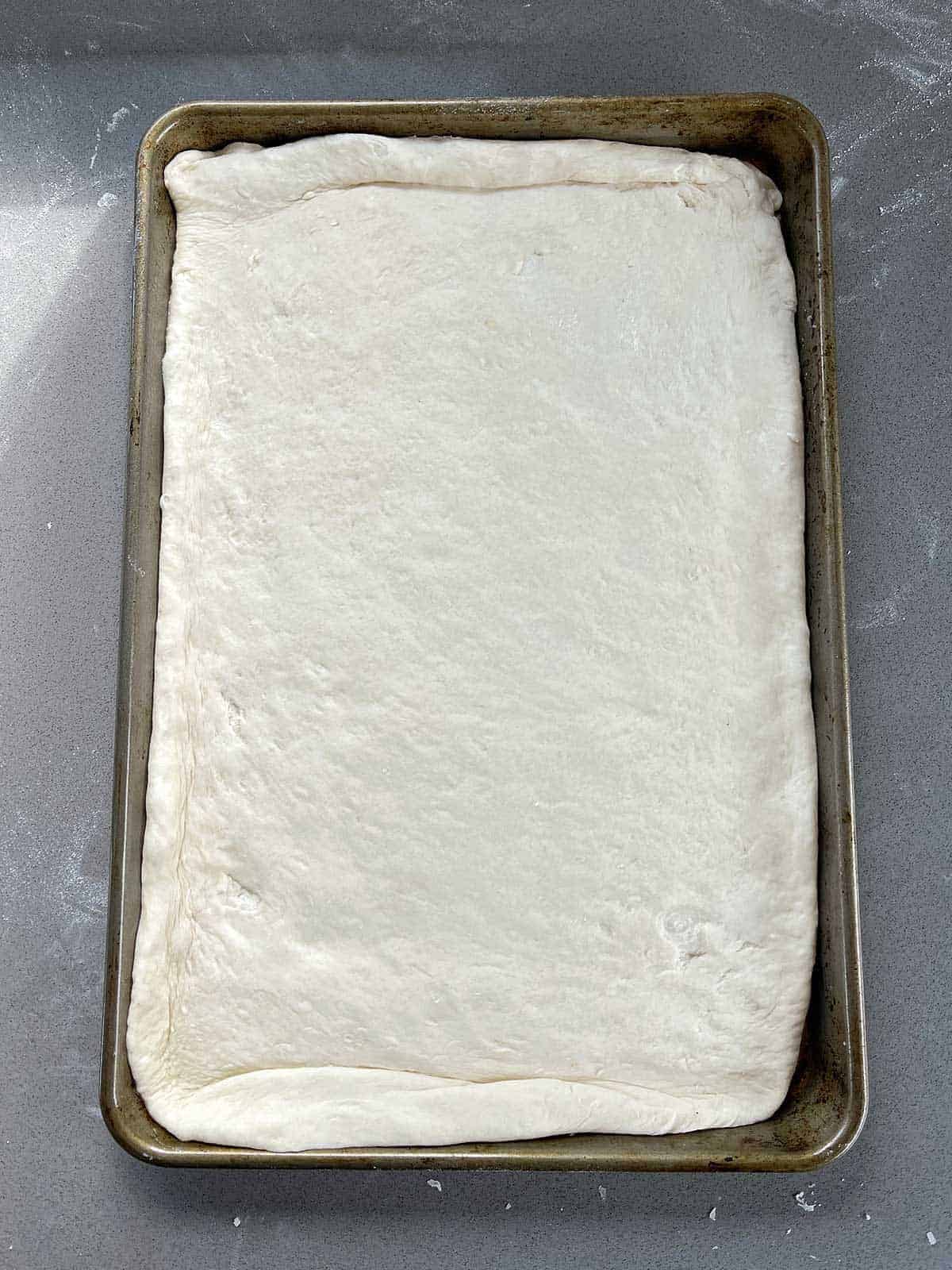 Uncooked, rolled out pizza dough sitting on a baking tray.