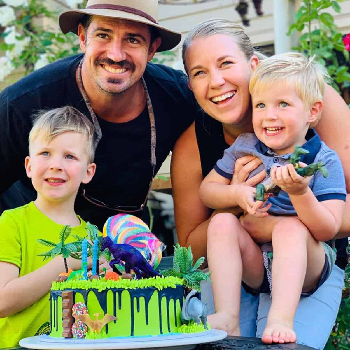 A family standing behind a green, dinosaur themed birthday cake.