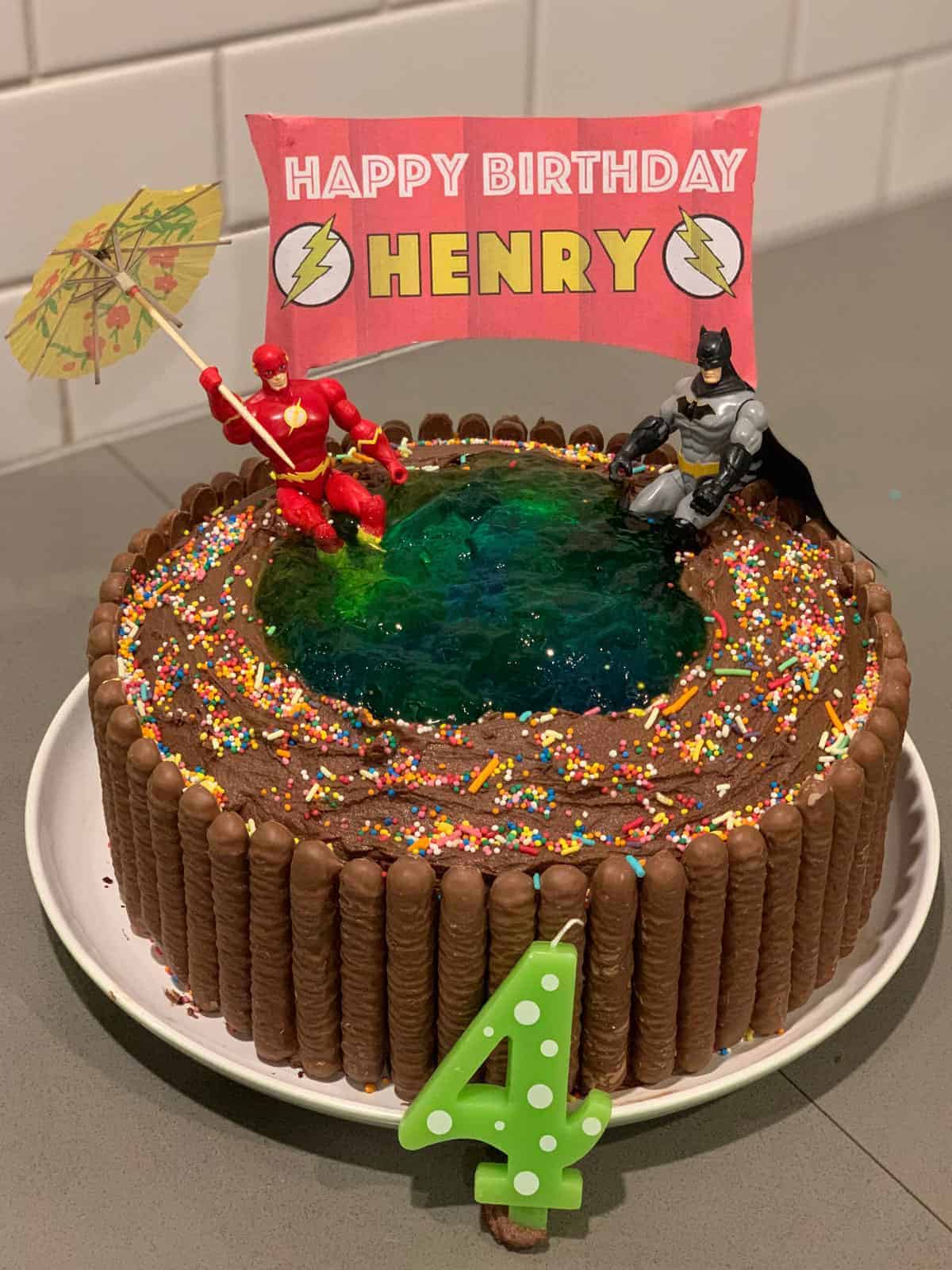 A chocolate birthday cake decorated to look like a swimming pool with super hero toys in it.