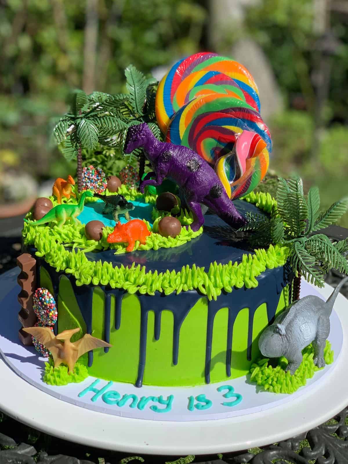 A green birthday cake decorated with dinosaur figurines and lollipops