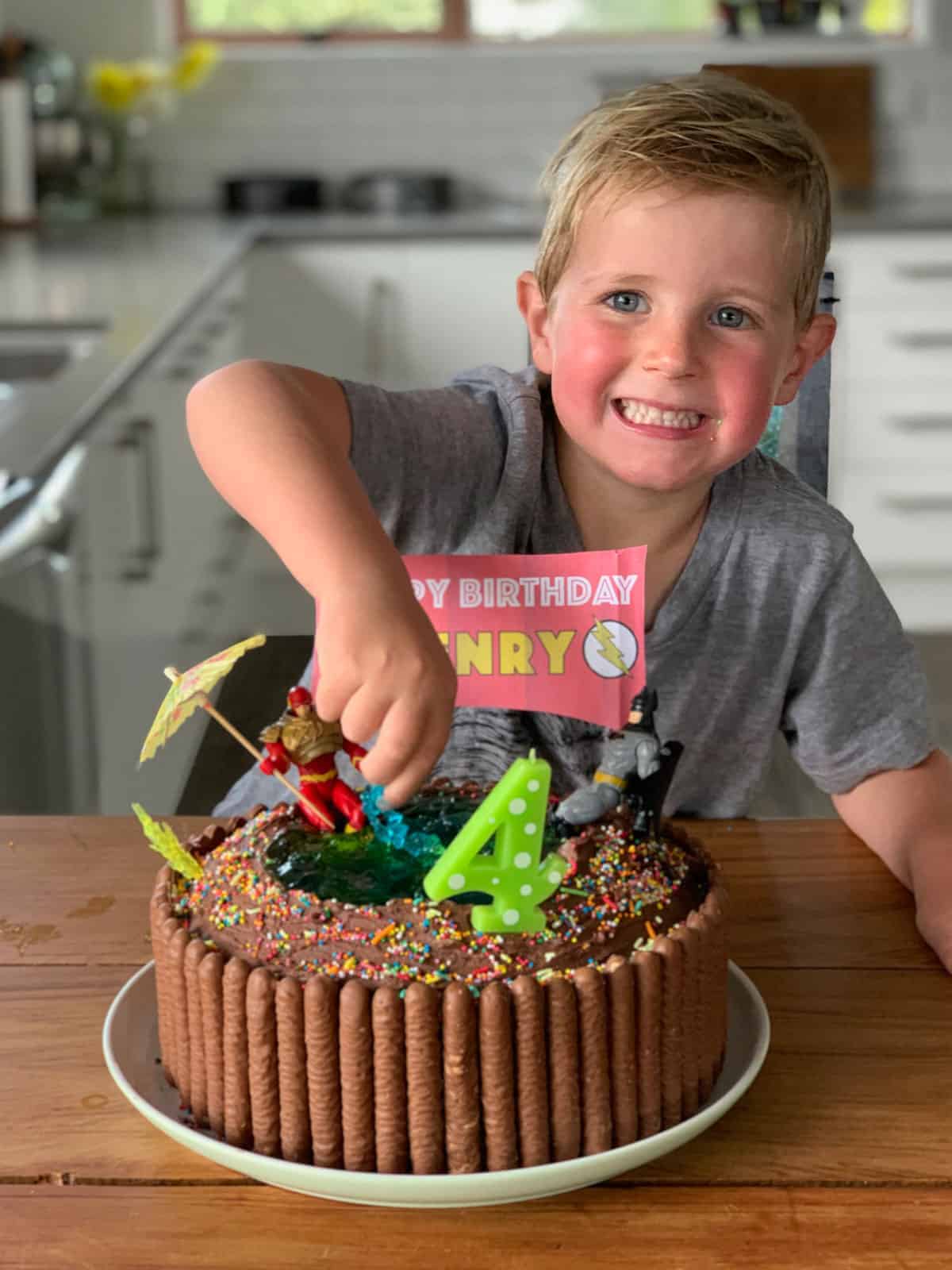 a boy standing behind a 4th birthday cake decorated to look like a swimming pool