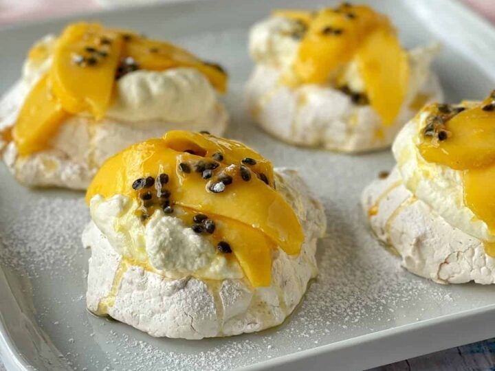Mini pavlovas on a white plate with sliced mango and passionfruit on top