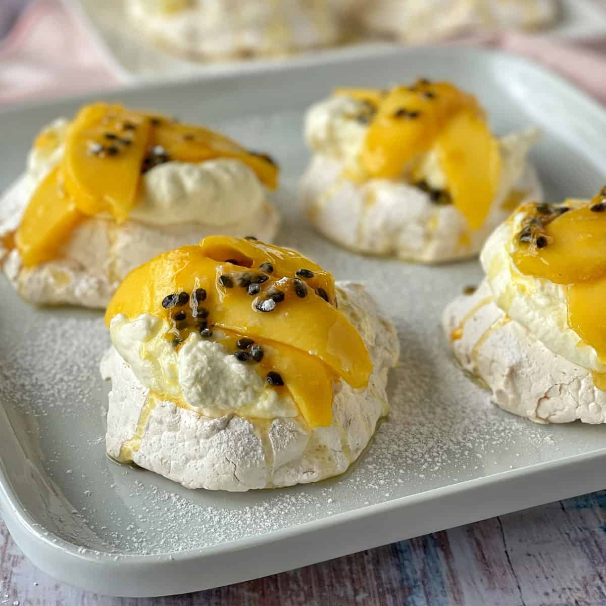 Mini pavlovas on a white plate with sliced mango and passionfruit on top