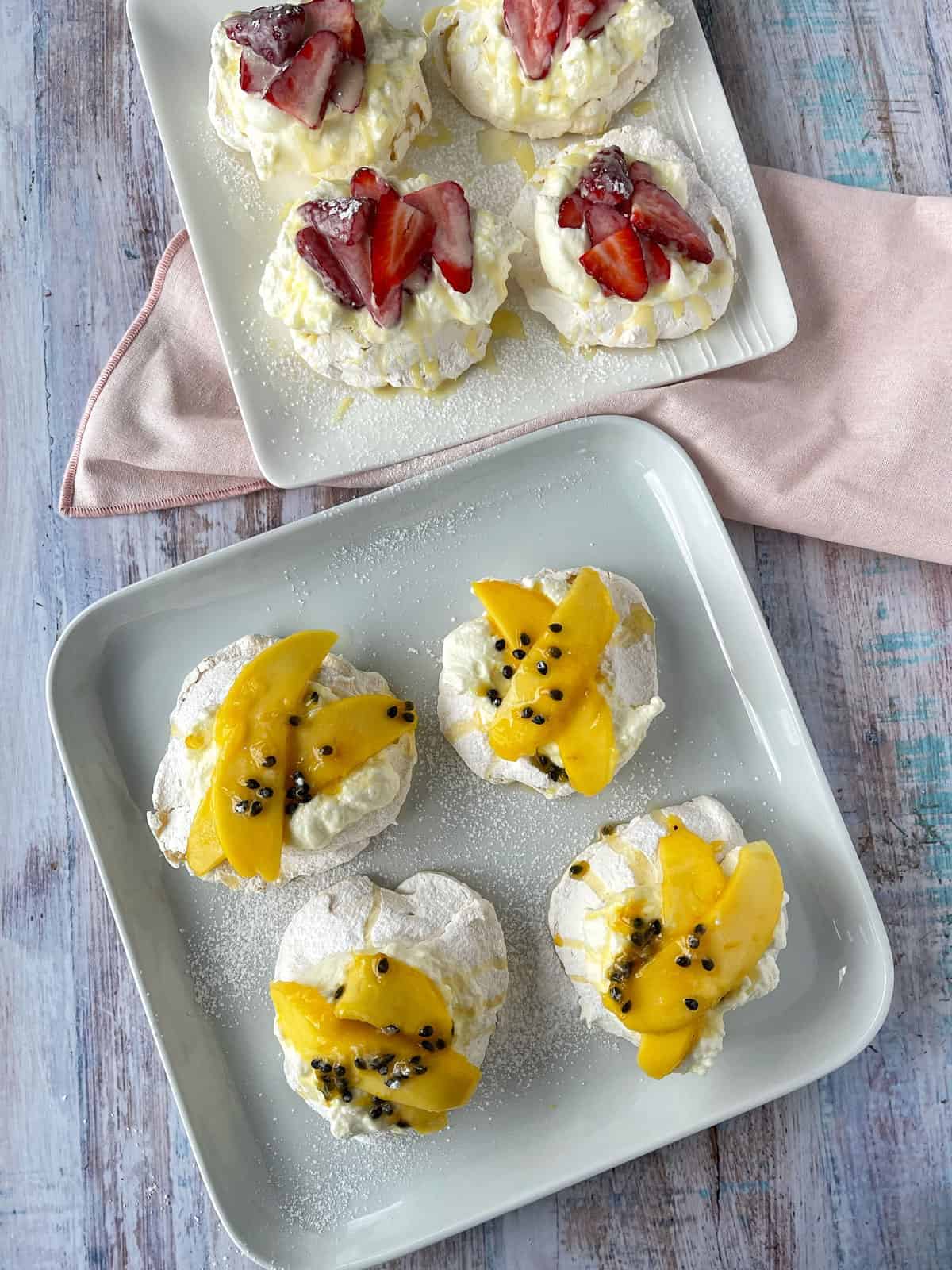 Birds eye view of mango and and strawberry pavlovas sitting on white platters