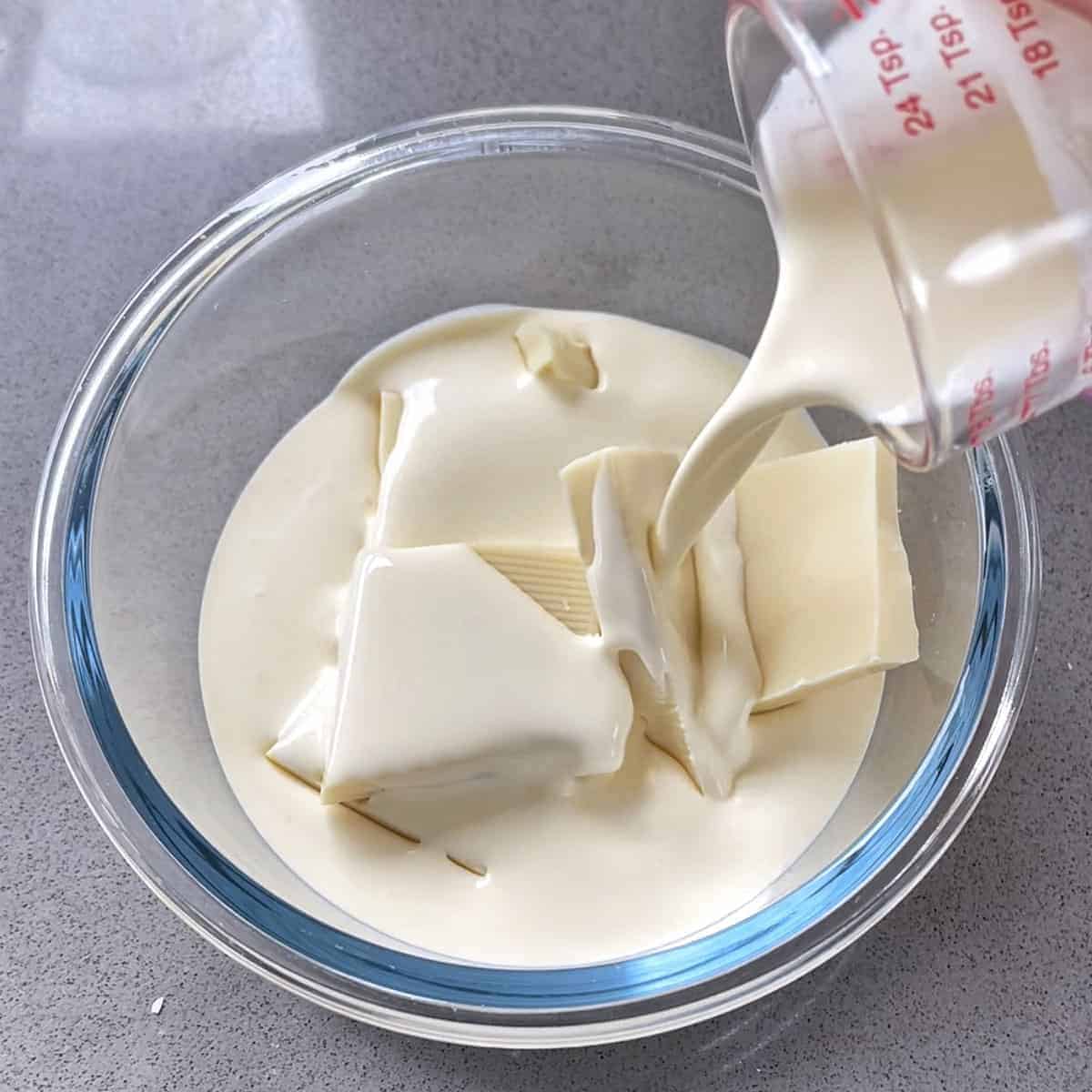 Cream being poured into a glass bowl with white chocolate in it.