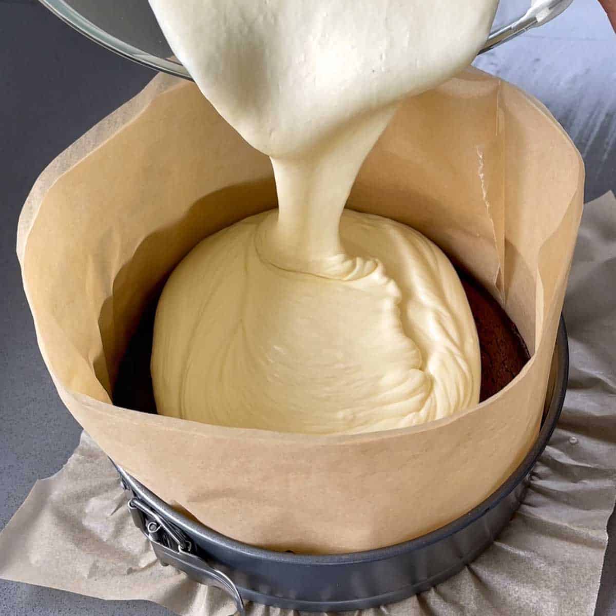 white chocolate mousse being poured into a lined cake tin.