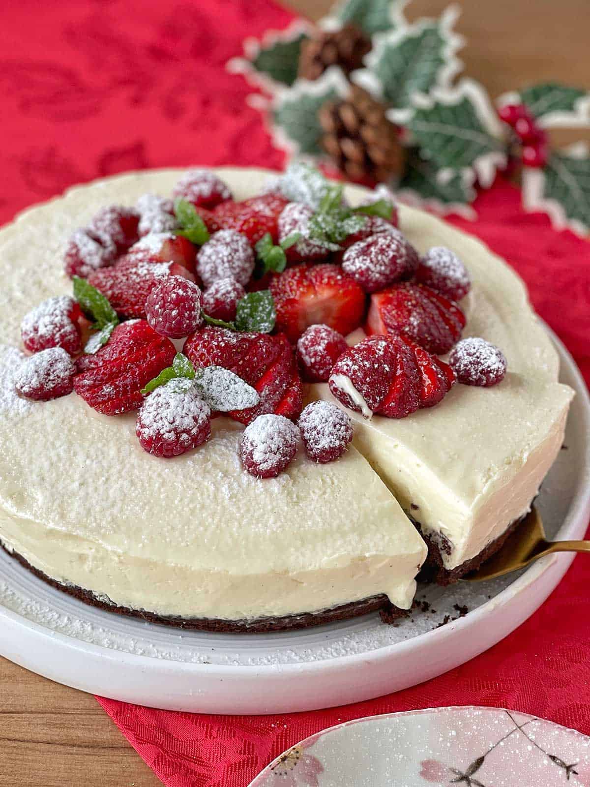 A close up of White Chocolate Mousse Cake sitting on a white plate with Xmas decorations.