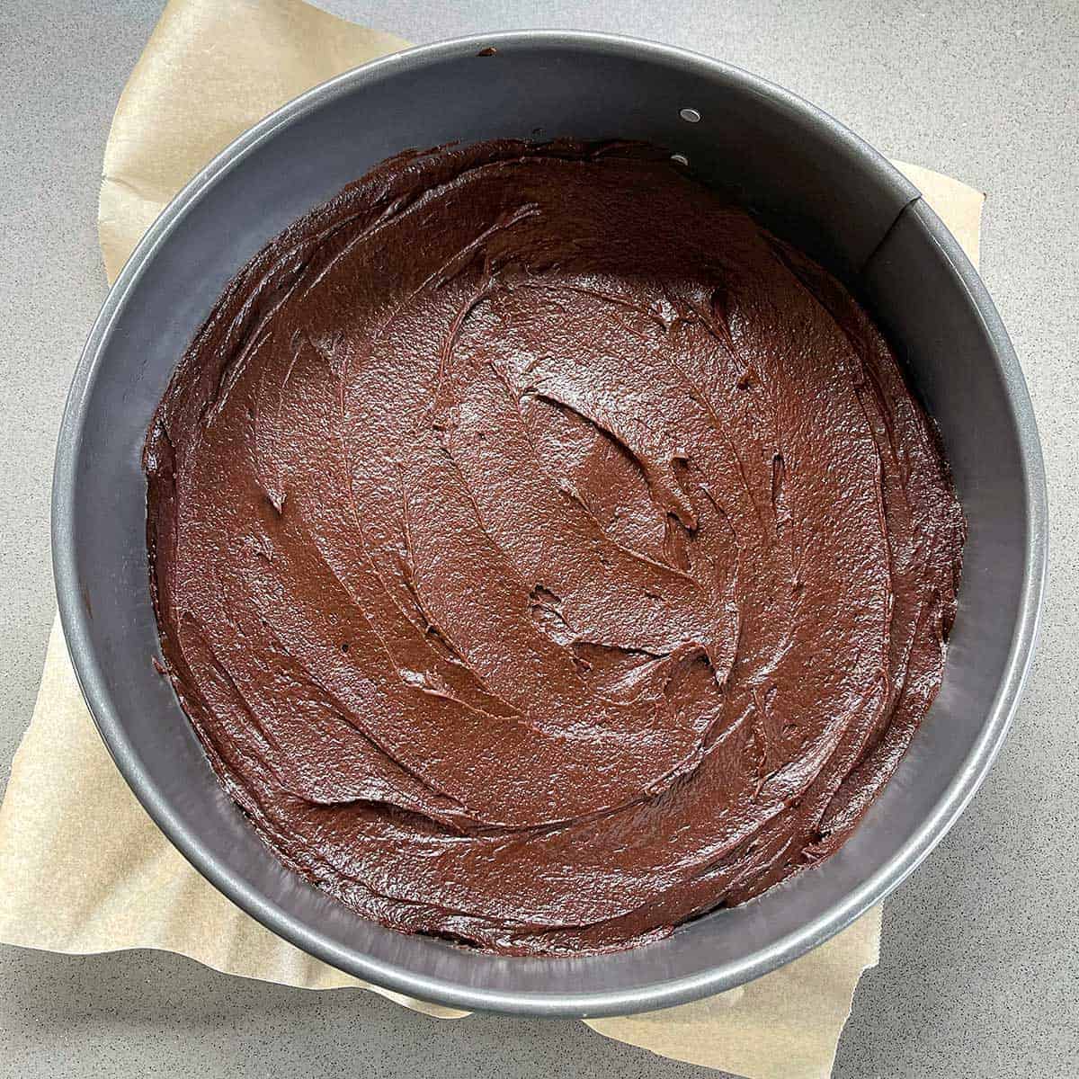 A cake tin with chocoalte cake batter sitting on a grey bench.