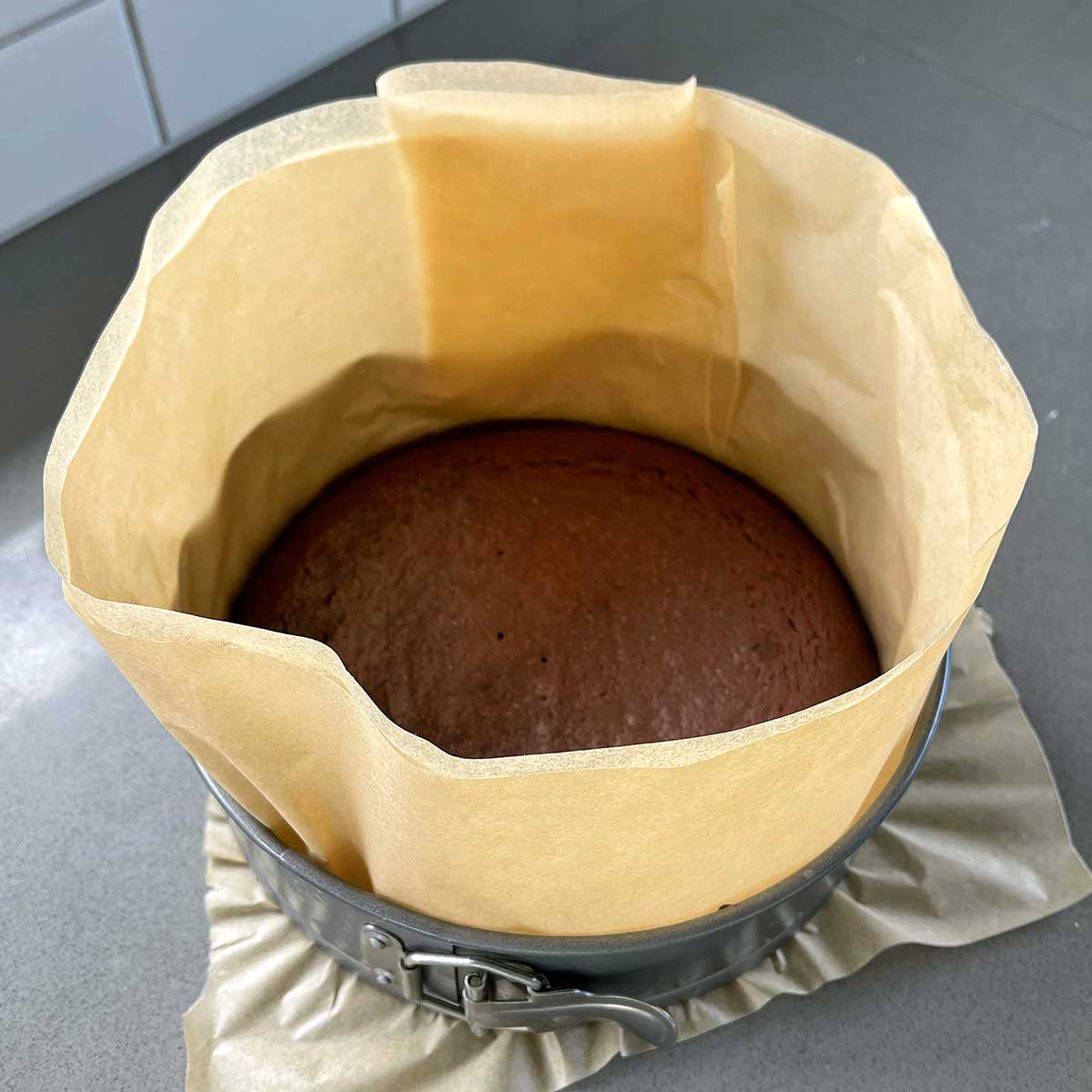 A cooked chocolate cake in a tin lined with baking paper.