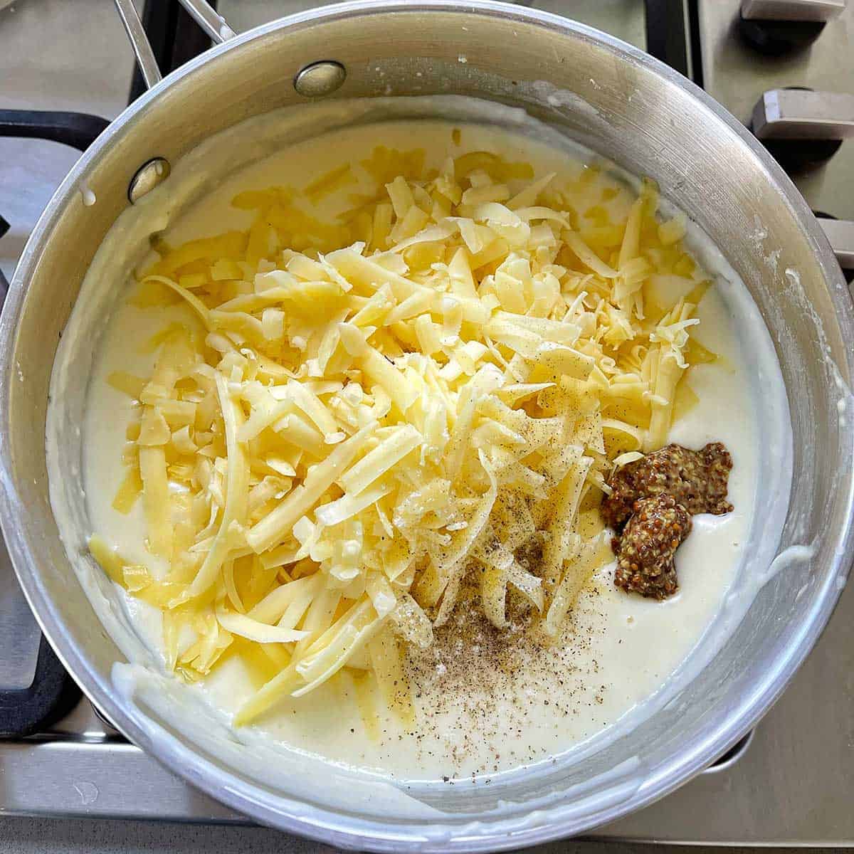 Cheese and mustard being added to a saucepan with cheese sauce in it