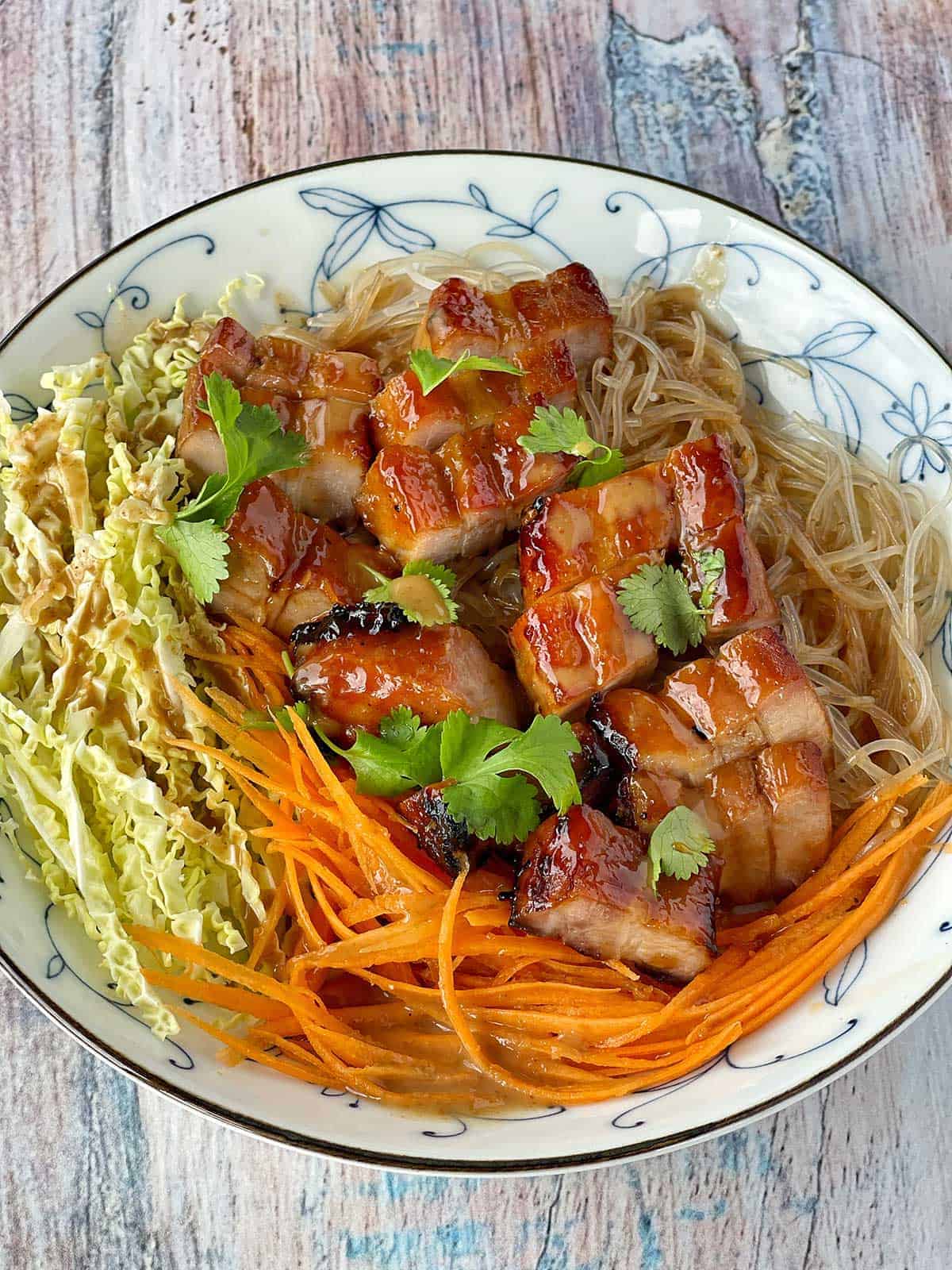 A close up of Chinese Pork with Noodles served in a white bowl.