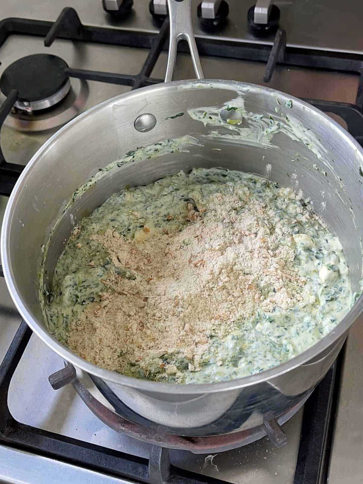 Creamy Spinach dip being made in a saucepan on the stove top.