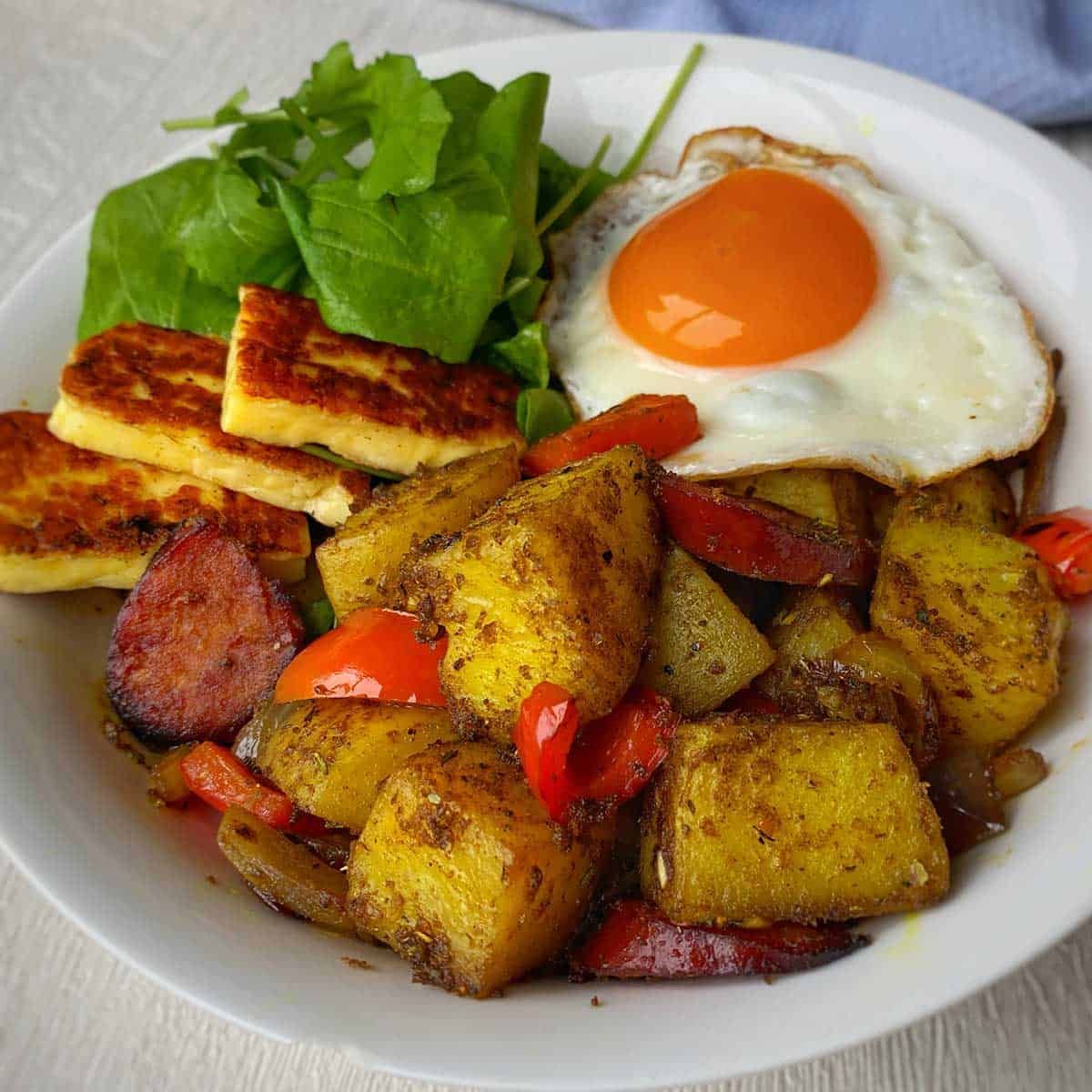 A close up of Haloumi & Chorizo Curried Potatoes served in a white bowl.