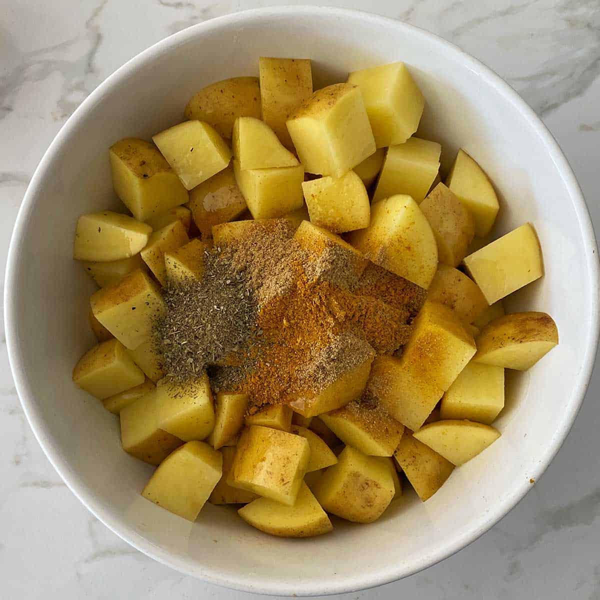 Spices in a bowl with cubed potatoes.