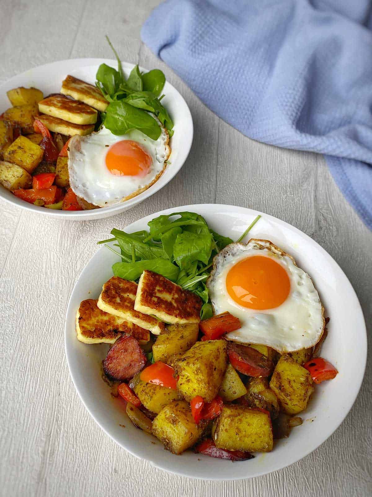 Two plates of Haloumi & Chorizo Curried Potatoes sitting on a grey bench.