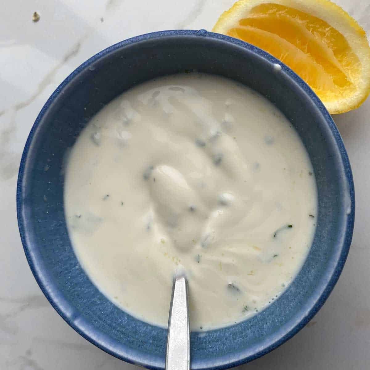 Mint yoghurt dressing a blue bowl next to a piece of lemon.