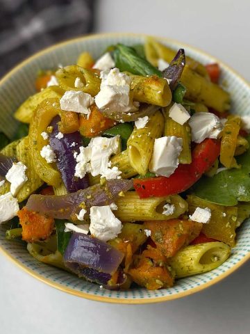 A close up of Roasted vegetable and pesto pasta salad in a white bowl on a bench.