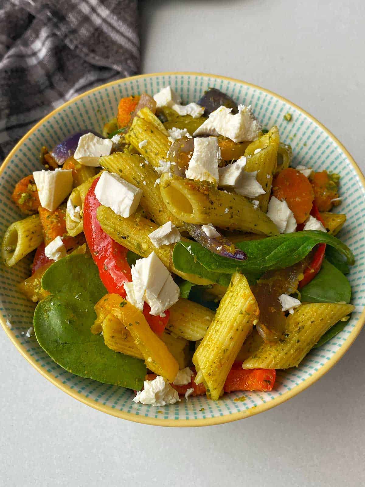 A close up of roasted vegetable and pesto pasta salad in a small bowl.