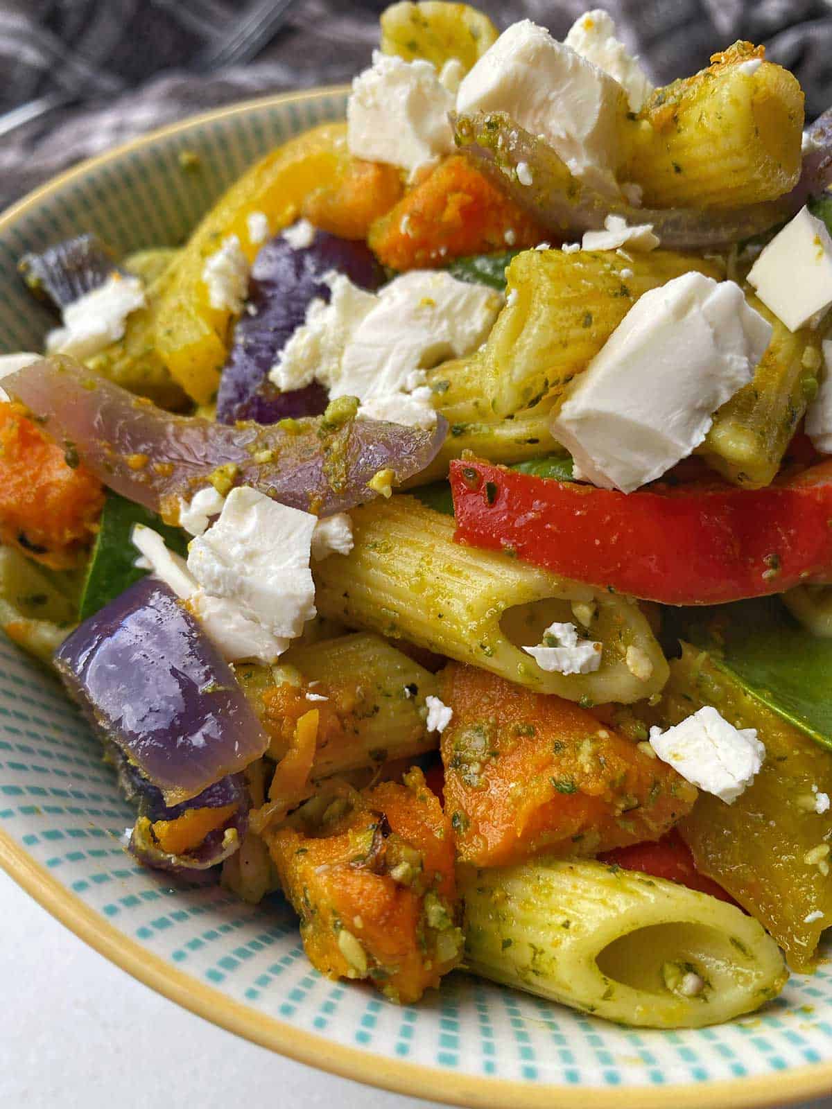 A close up of Roasted vegetable and pesto pasta salad in a white bowl.