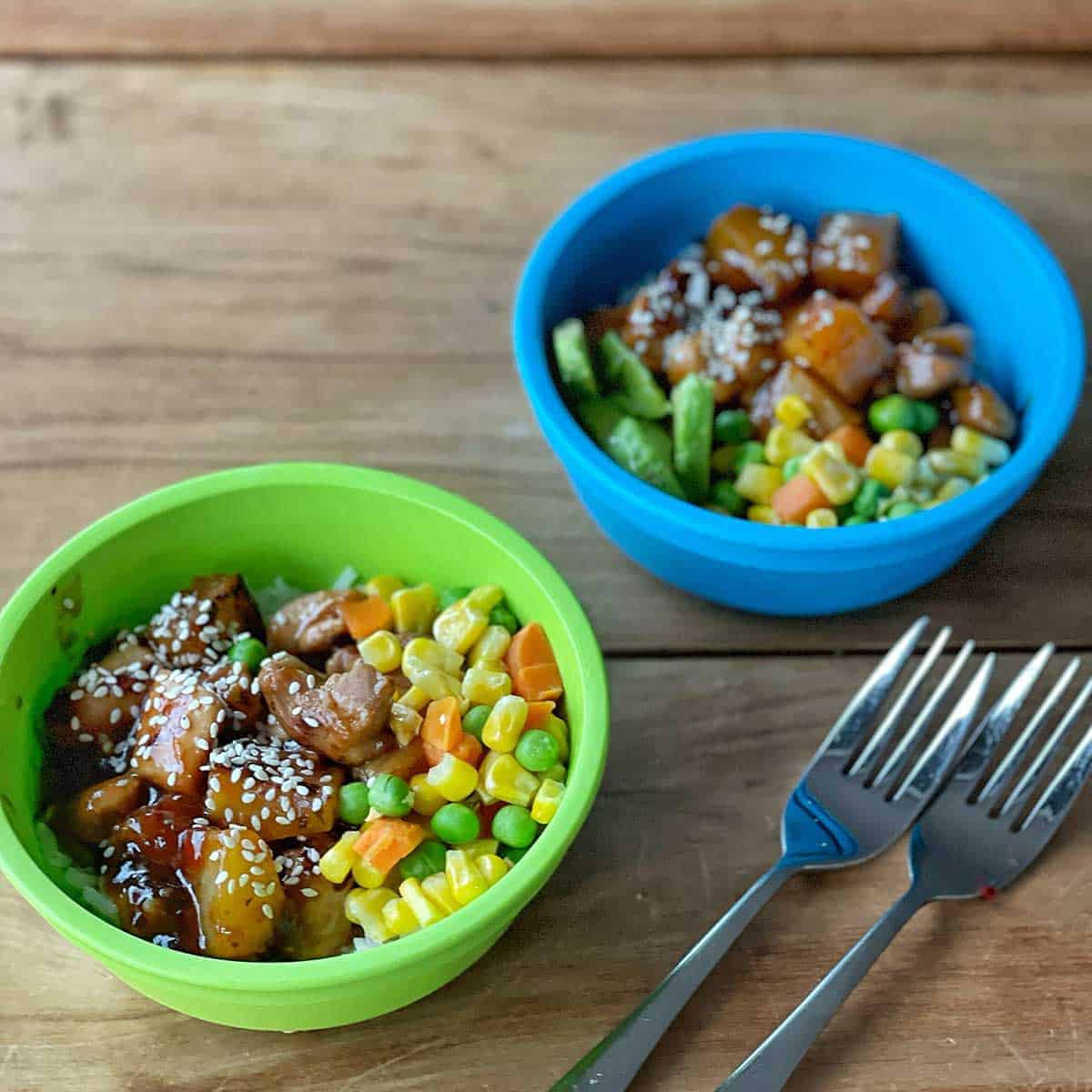 Two small servings of Sticky Pineapple Chicken in plastic blue and green bowls.
