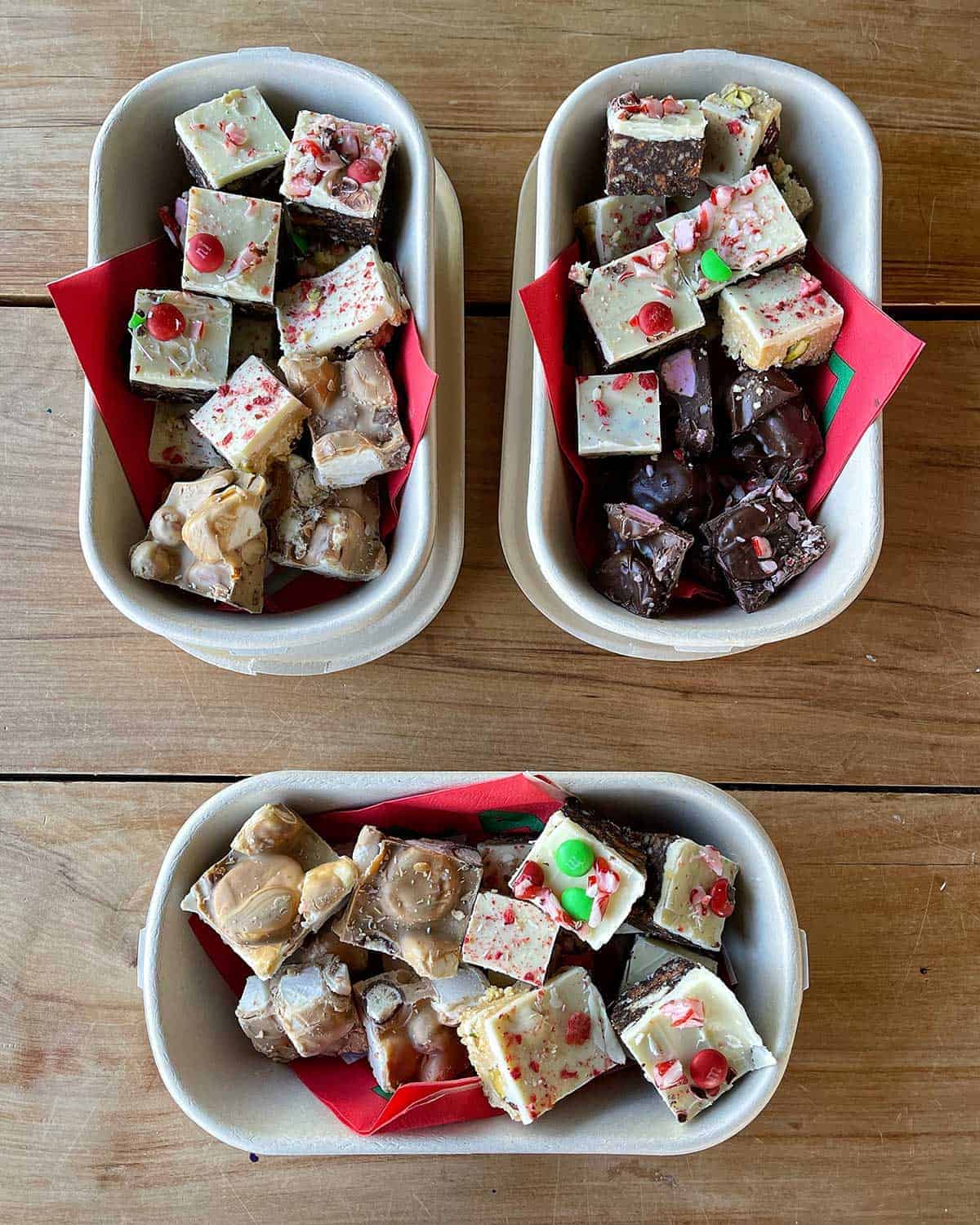 Three smaller container filled with different Christmas Treats sitting on a wooden bench.