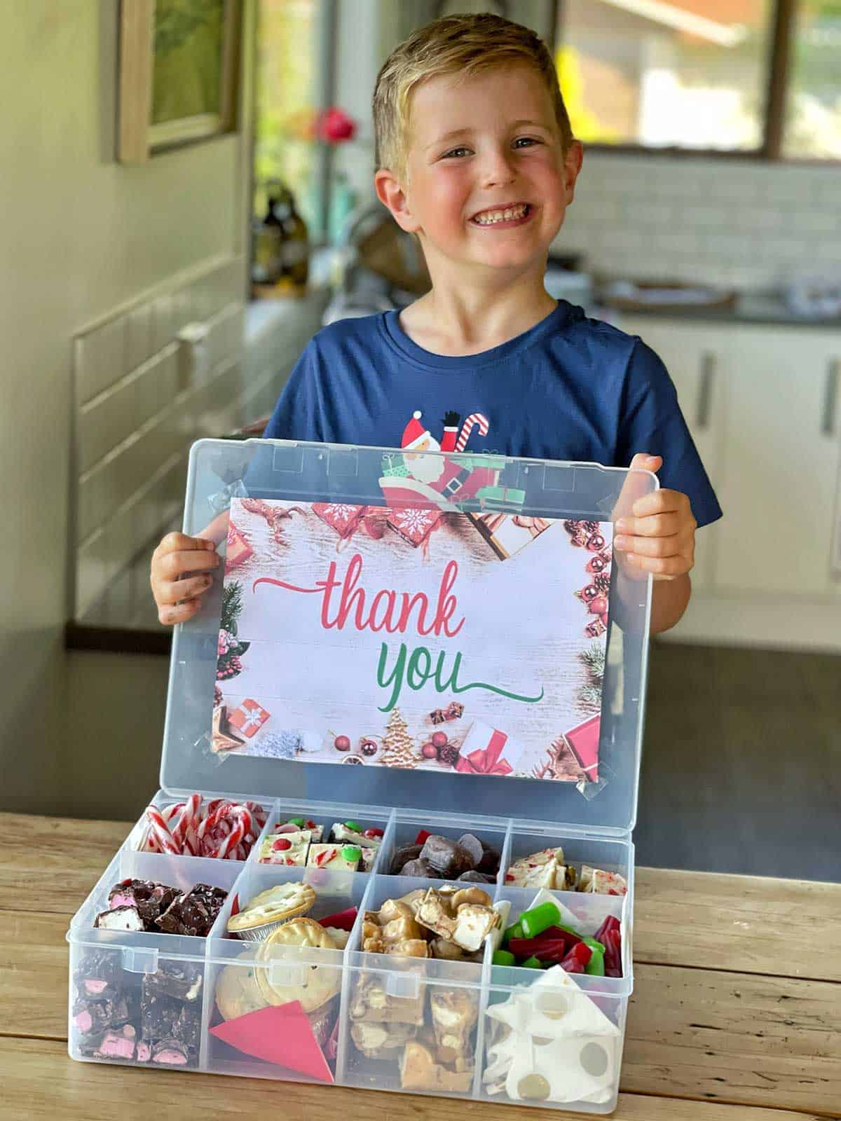 a boy standing behind a Christmas Treat box in a kitchen.