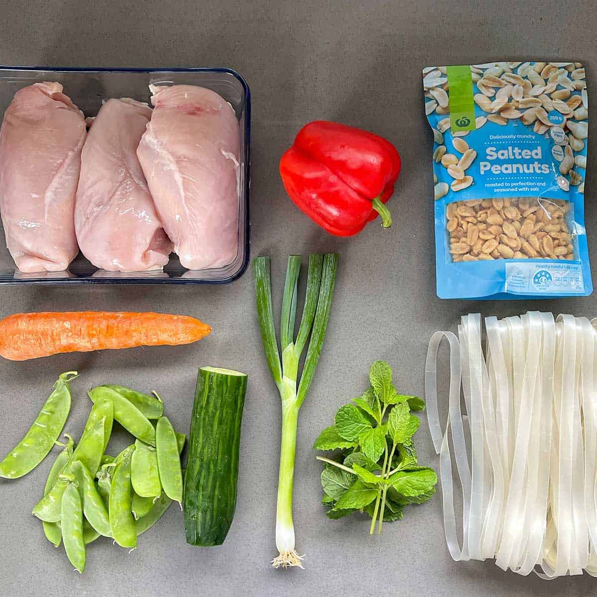 The ingredients for Thai Chicken Noodle Salad sitting on a grey bench.