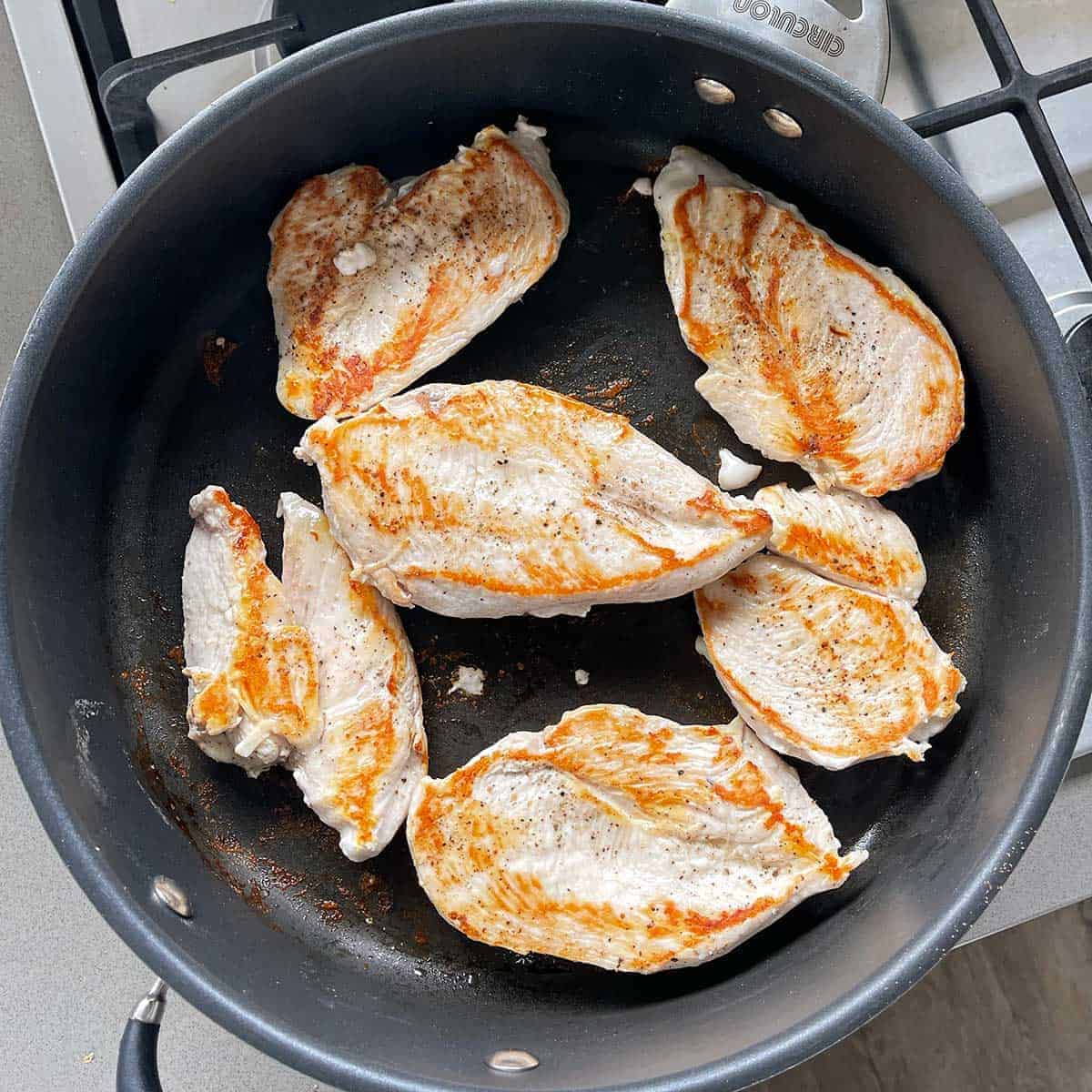 Chicken breasts cooking in a large pan.