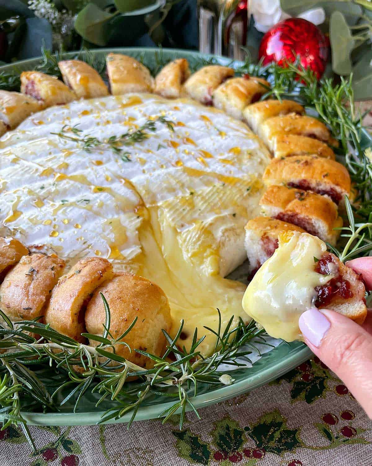 A hand pulling a piece of cheesy bread off the Brie Wreath.