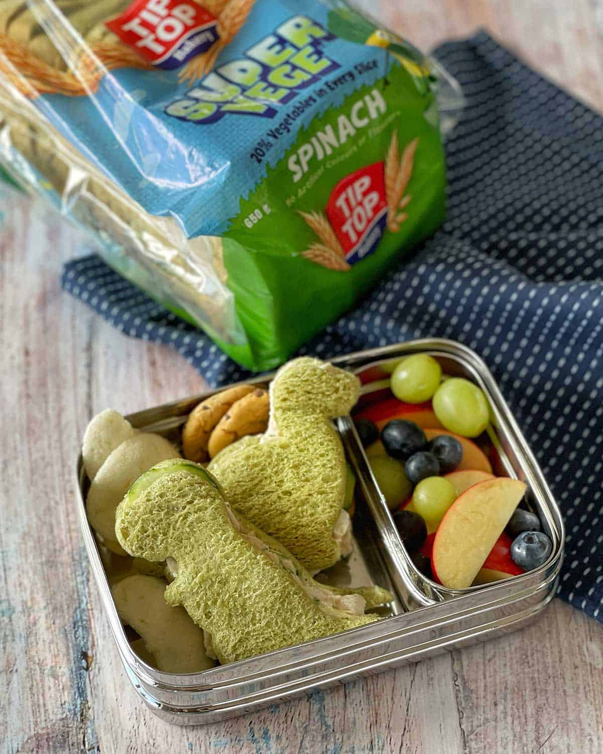 Dinosaur shaped Chicken Salad Sandwiches in a child's lunchbox next to a packet of sandwich bread.