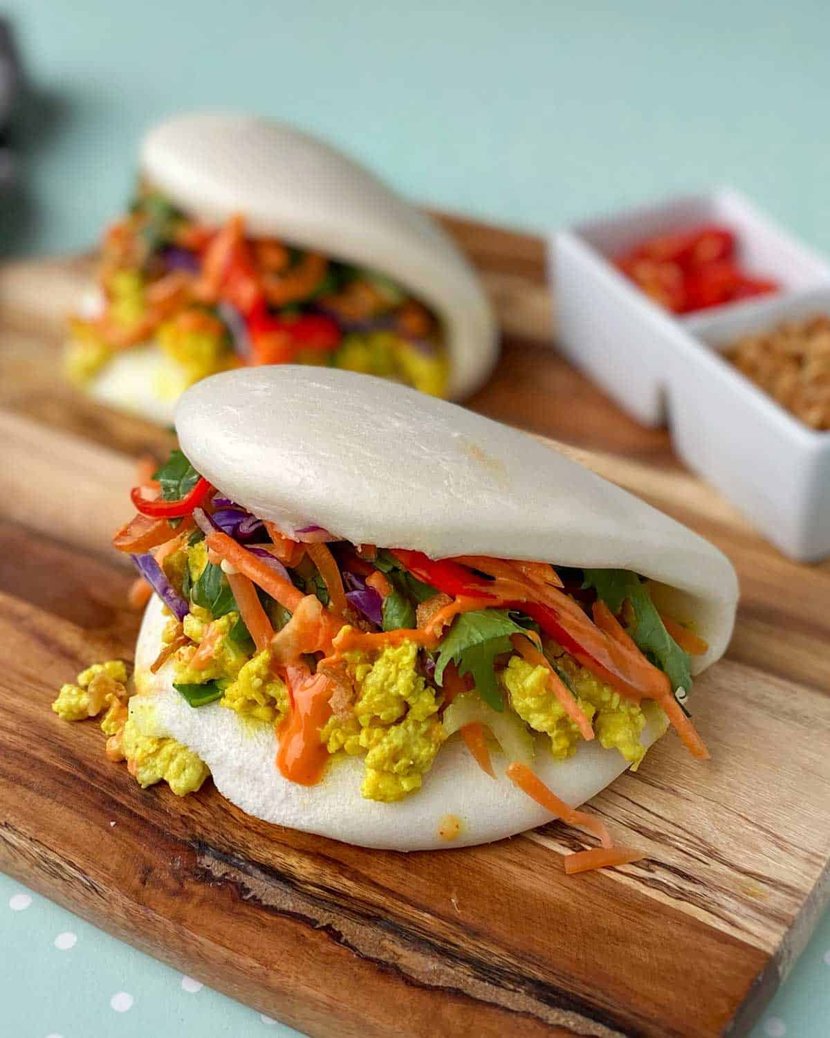 Two Coconut Chicken Bao Buns sitting on a wooden chopping board.