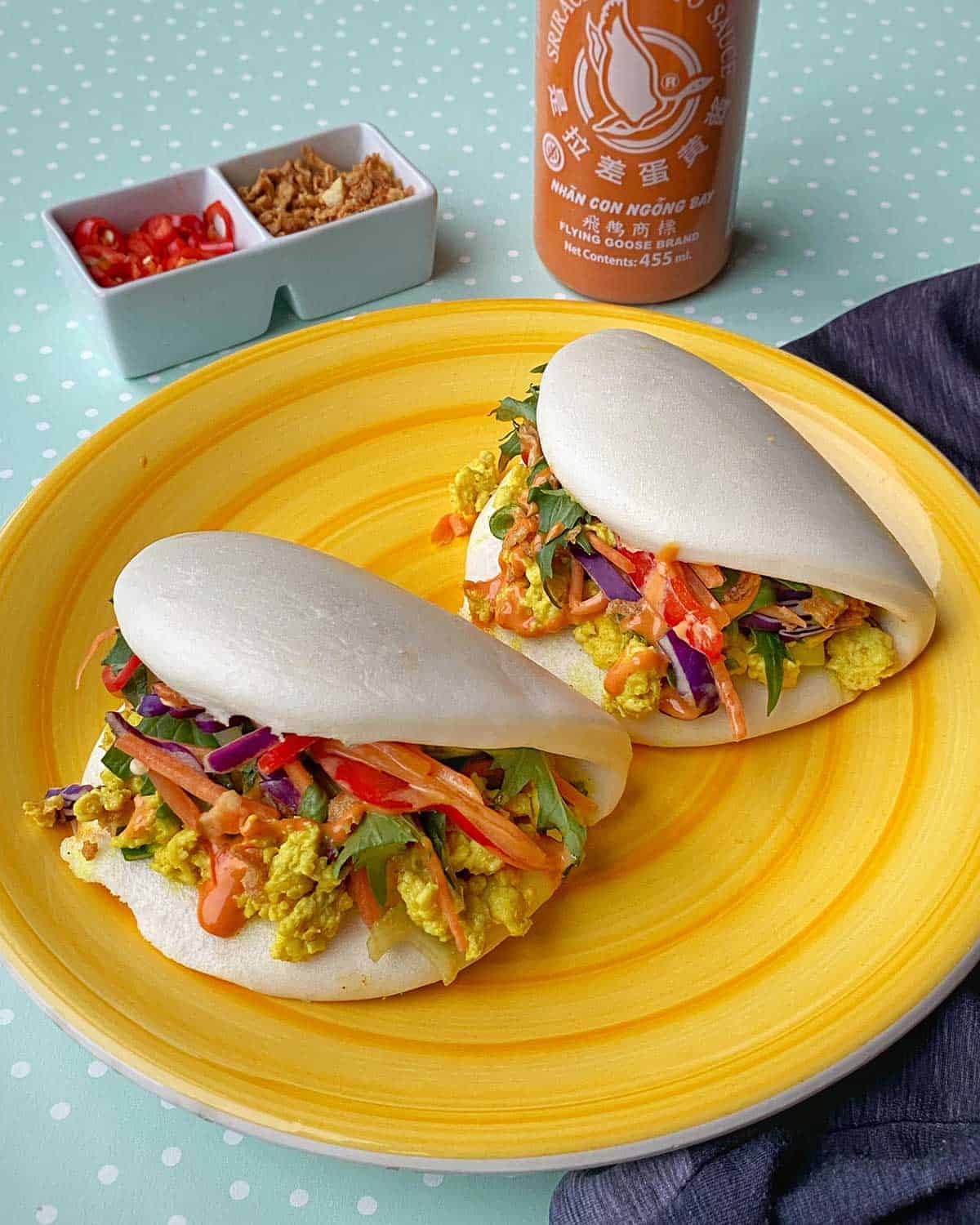 Coconut Chicken Bao Buns sitting on a yellow plate with condiments in the background.