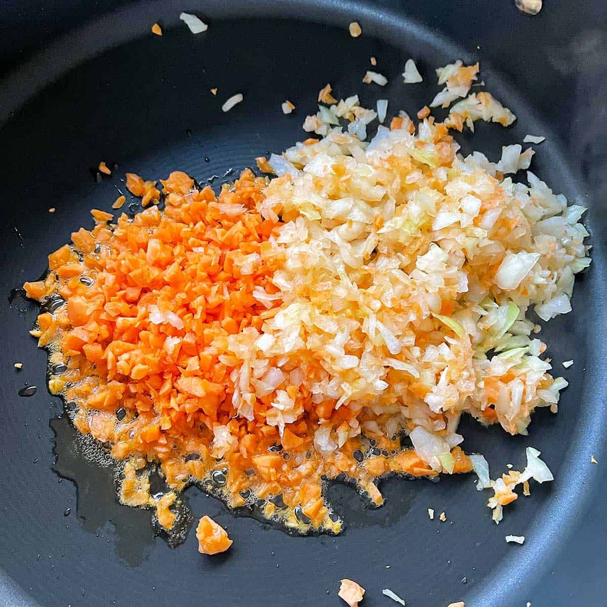 Diced carrot and onion cooking in a frying pa.