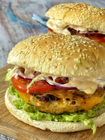 A close up of two Mexican Chicken Burgers sitting on a wooden chopping board.