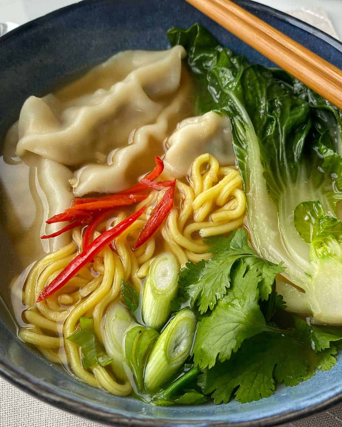 A close up of Dumpling Noodle Soup in a blue bowl.