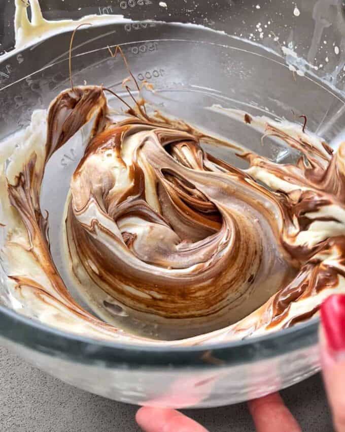 A glass bowl cradles a smooth, marbled mixture of melted chocolate and cream being stirred, reminiscent of the decadent filling found in Easter Cheesecake Cups.
