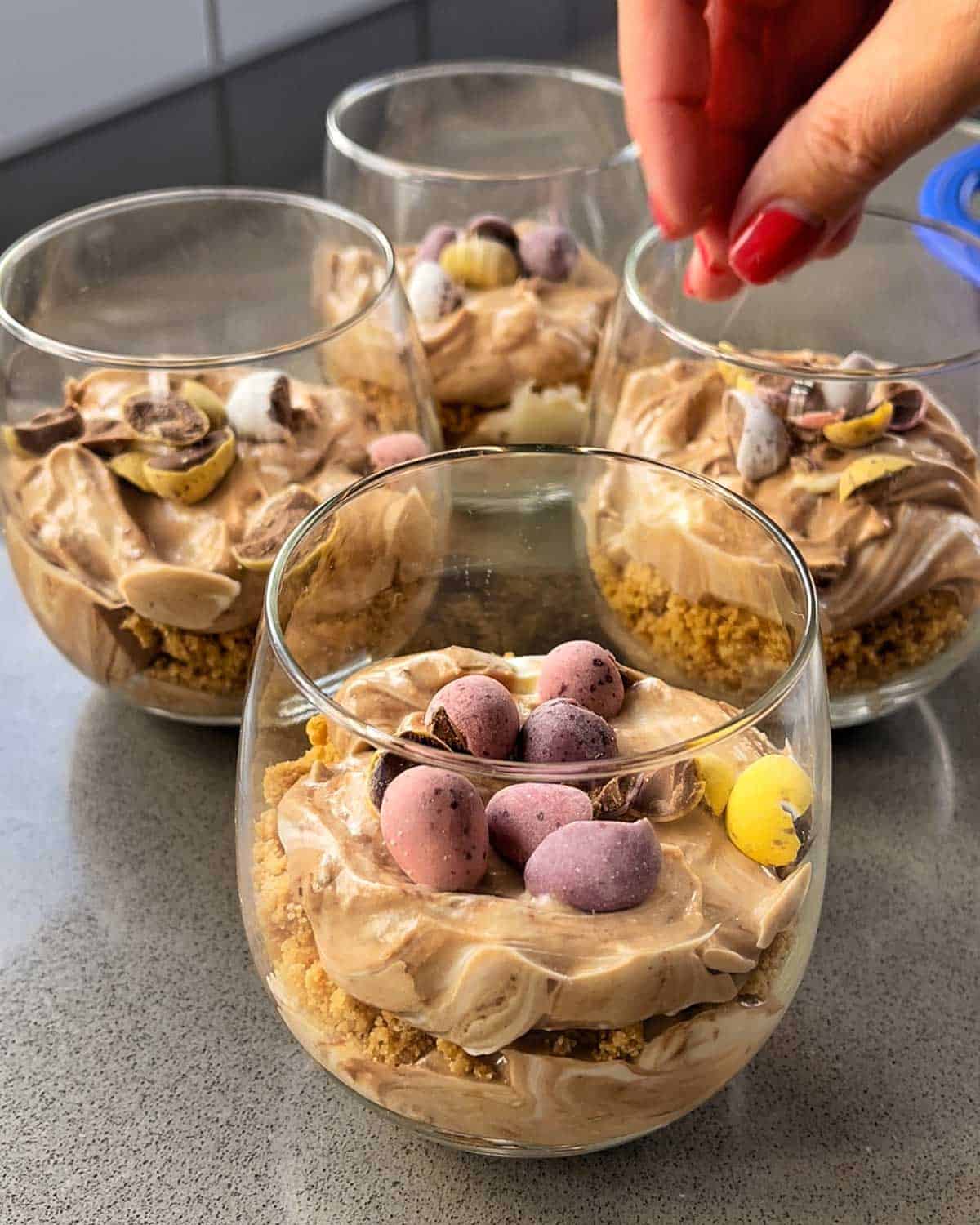 A hand sprinkling chopped eggs on top of cheesecake cups.