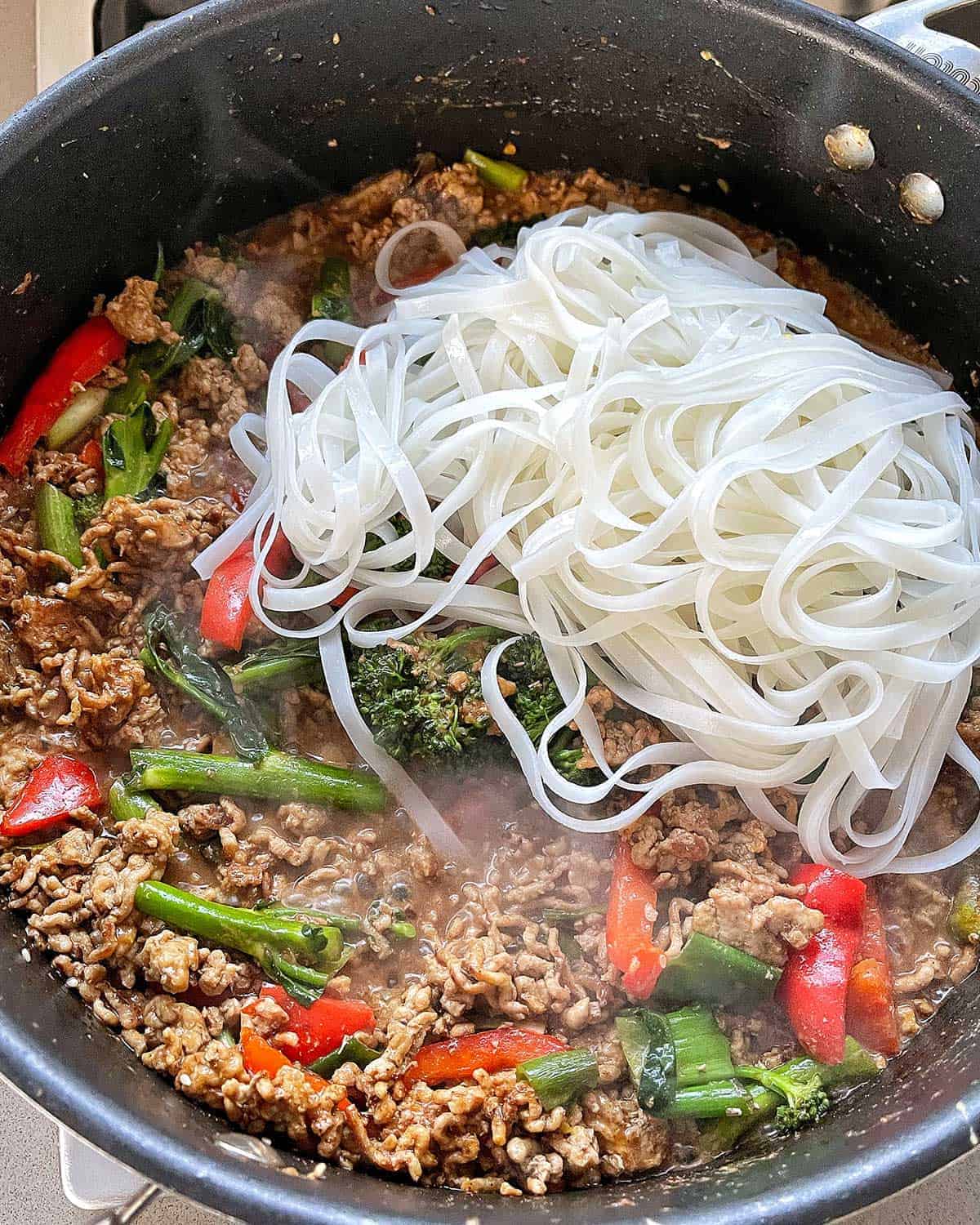 Noodles and pork mince cooking in a large frying pan.