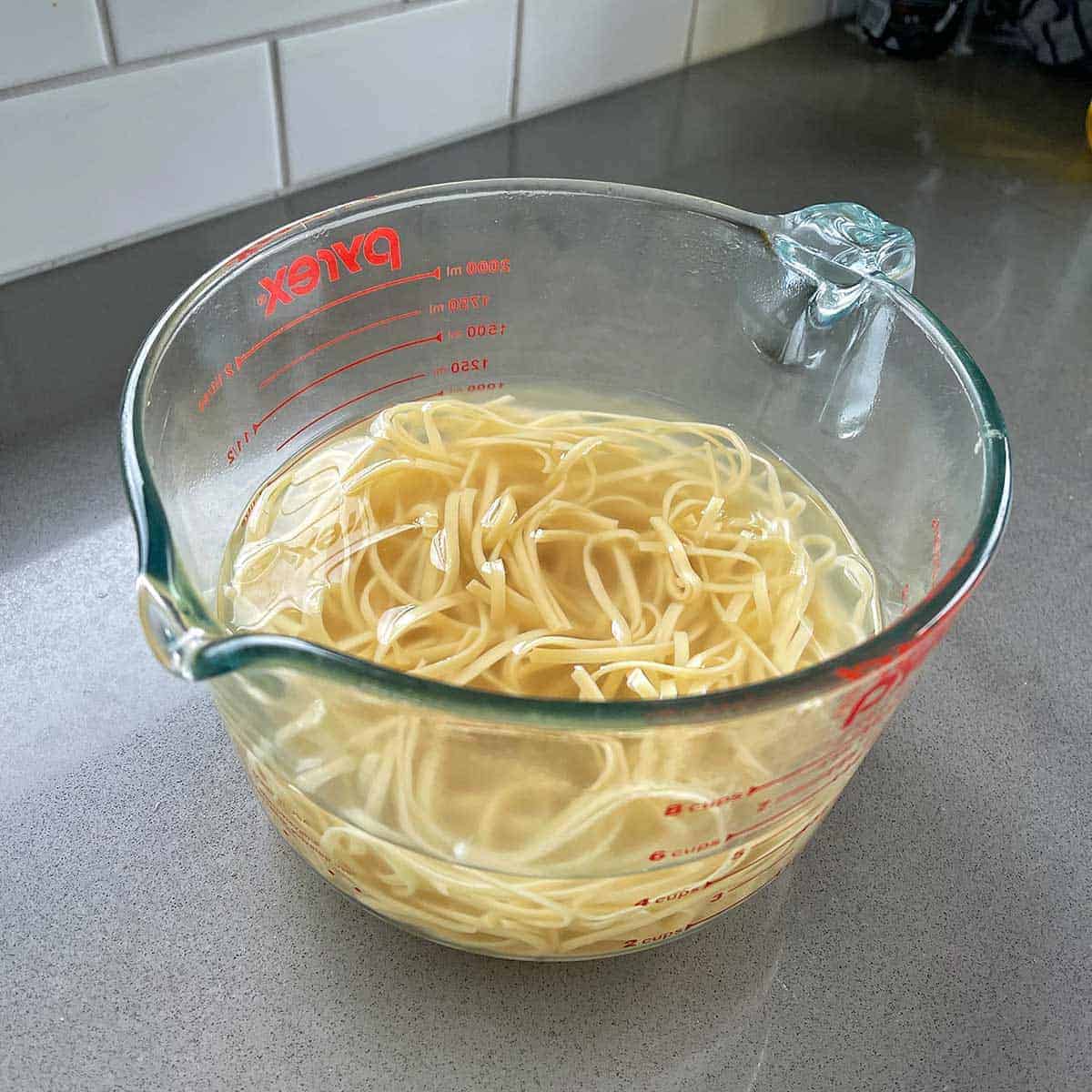 Noodles cooking in a glass jug with boiling water.