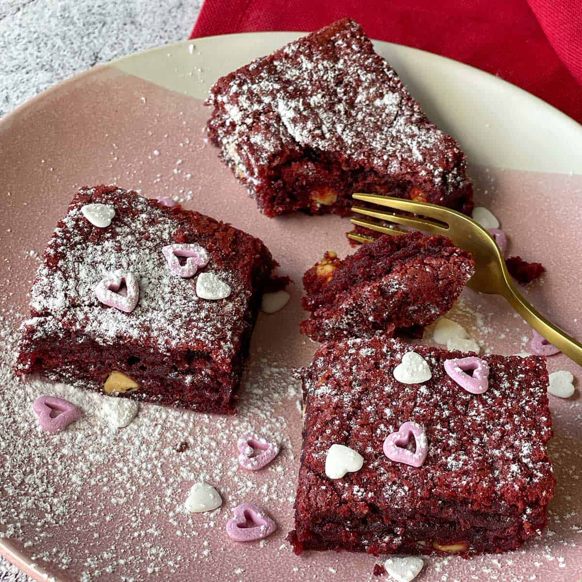 3 pieces of red velvet brownie on a pink plate.