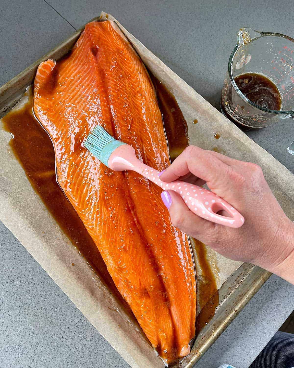 A hand brushing a fillet of salmon with a honey glaze.