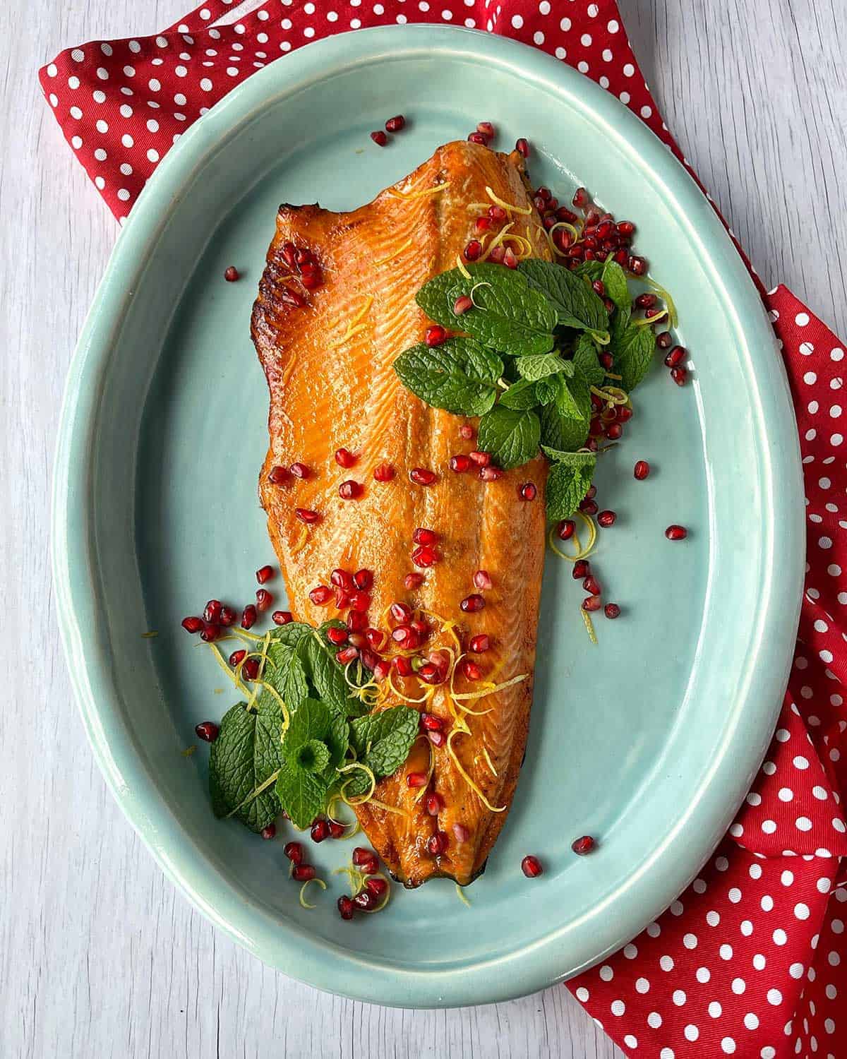 Cooked salmon garnished with pomegranate seeds and mint on a blue platter.