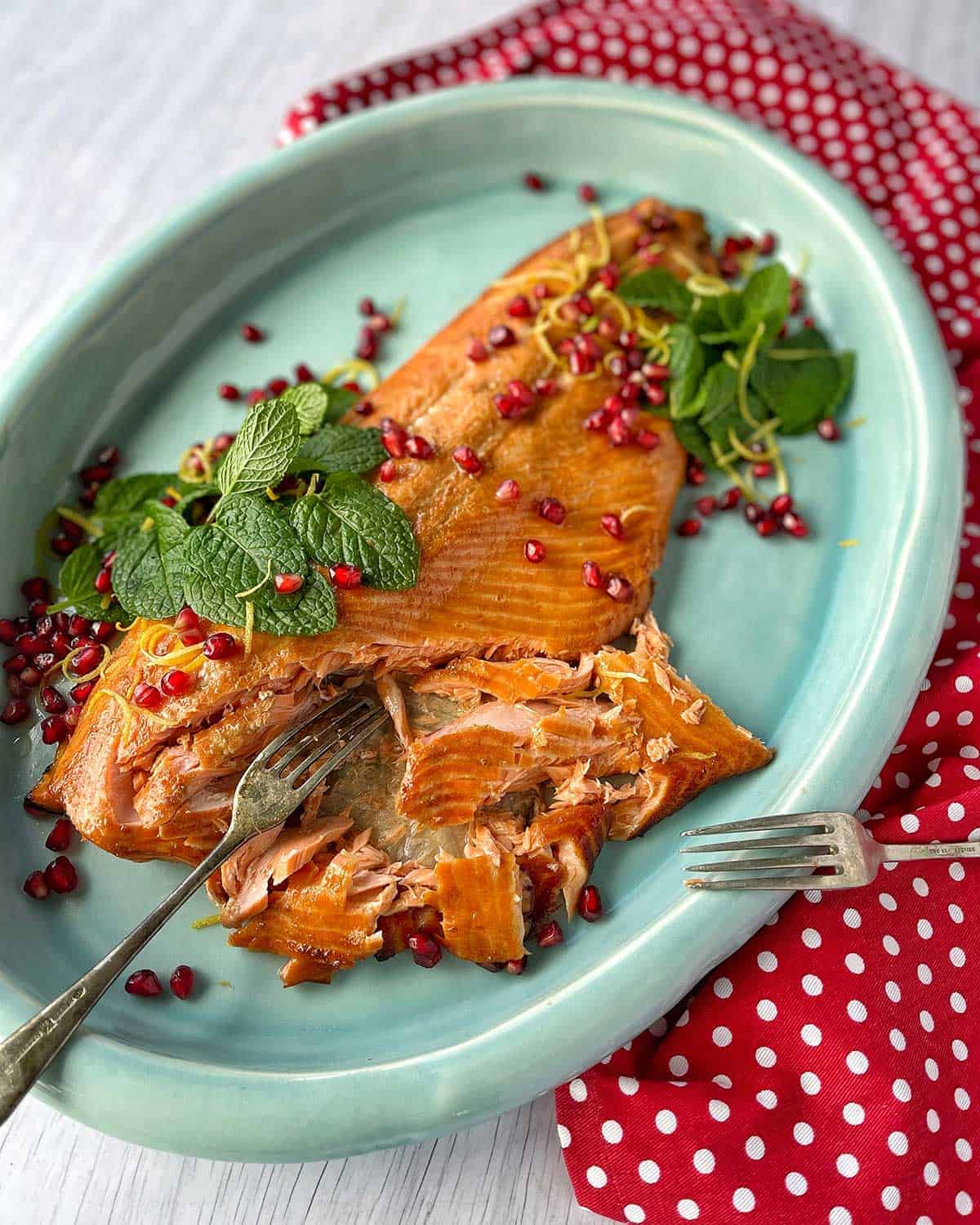 A whole baked salmon on a blue platter with two forks resting on the side.