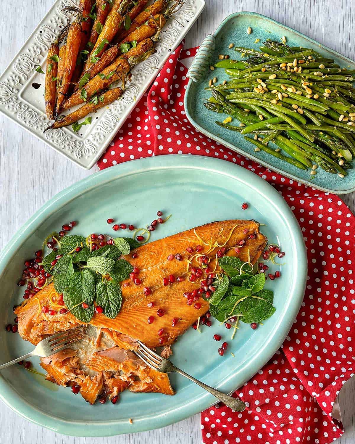 Whole Baked Salmon next to plates of glazed carrots and green beans.